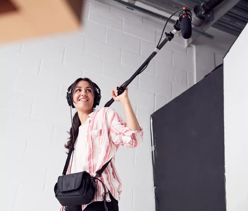 Mujer joven aprendiendo sonido directo con micrófono boom durante un curso de producción audiovisual