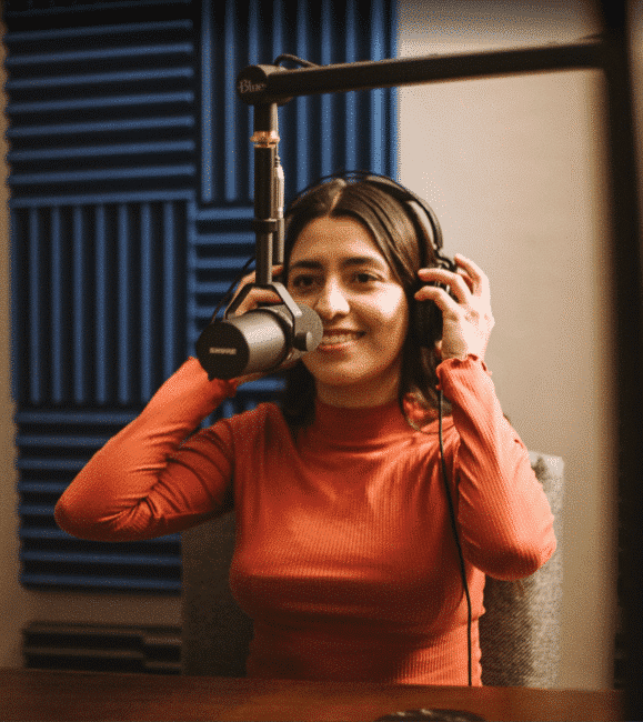 Mujer ajustando audífonos frente a micrófono Shure durante sesión de grabación de podcast en estudio profesional de Soonus Guadalajara.